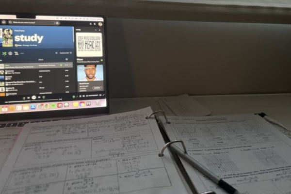 A laptop displaying a study playlist sits next to a binder full of classwork. Music has been shown to improve focus and productivity when completing tasks, such as school assignments. 